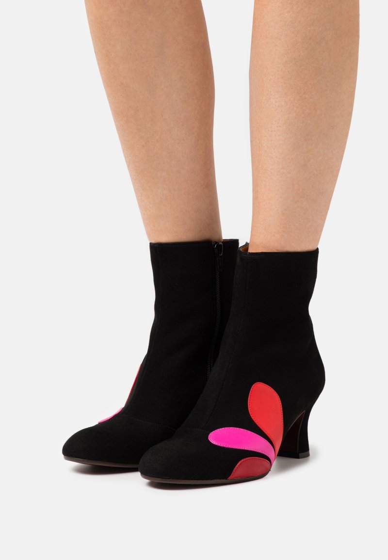 Bottes noires montantes mi-mollet à talons avec fermetures éclair latérales, ornées de motifs en forme de pétales rouges et roses près des chevilles sur un fond uni.