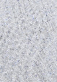 Lys grå strikket stoff med subtile blå og lilla fnugg vevd gjennom, som viser detaljert nærbilde av tekstur.