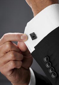 Svart dressjakke med en hvit skjorterm featuring en svart mansjettknapp. Skjortermet er pent presset og hånden justerer mansjettknappen.