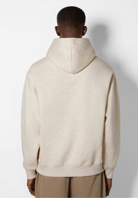 Beige huvtröja med mjuk textur. Har ribbade ärmslut och krage, samt en sömlös huva. Bakifrån visar den en avslappnad passform.