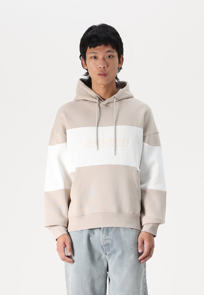 Sweatshirt à capuche en blocs beige et blanc, avec un tissu texturé, une poche kangourou et un logo de marque brodé sur la poitrine.