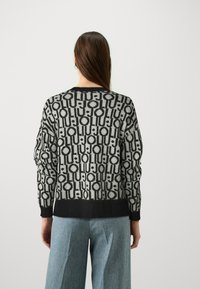 Maglione lavorato a maglia in grigio e nero con un motivo geometrico; presenta un orlo e polsini a coste, e una vestibilità morbida.