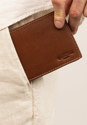 Brown leather wallet partially visible from a pocket, featuring a textured surface, contrasting stitching, and embossed branding on one corner.