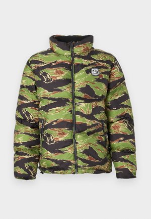 Kamalna puhovka z elementi kamuflaže v zeleni, črni in rjavi barvi z visokim ovratnikom in zadrgo. Na levi strani prsnega dela ima našitek z logotipom.