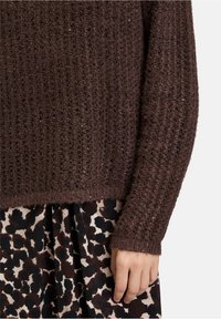 Bruine gebreide trui met een gestructureerde afwerking en subtiele glans, gedragen over een gemarmerde zwart-beige rok met een luipaardprint.