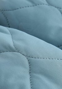 Tissu matelassé bleu clair avec une surface texturée, présentant des accents cousus formant un motif en losange. Apparence douce et lisse.