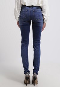 Jeans ajustados azules con una textura suave, diseño de cinco bolsillos y costuras traseras distintivas, combinados con zapatos de tacón alto puntiagudos.