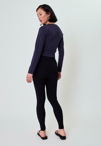 Langermige, donkergrijze top met een aansluitend ontwerp, gecombineerd met hoge zwarte leggings. Model draagt zwarte teenslippers. Eenvoudige, gladde textuur.