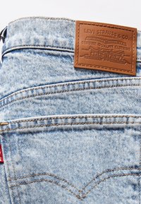 Gros plan d'un jean en denim bleu montrant une poche arrière avec une couture orange et une étiquette en cuir marron de la marque Levi Strauss & Co.