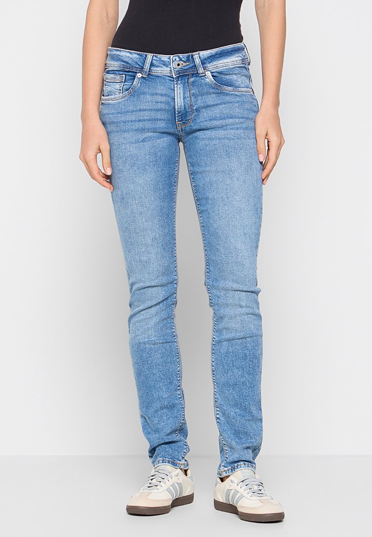 Helle blaue Jeans aus Denim, mit fünf Taschen, einem Reißverschluss und einem Slim-Fit-Design. Kombiniert mit beigen Sneakers.