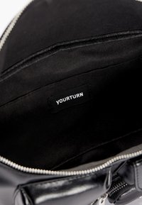 Czarna skórzana torba wewnątrz z gładką fakturą, z zamknięciem na zamek błyskawiczny na górze oraz metką z napisem "YOURTURN" w białym kolorze.