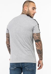 Gray short-sleeve t-shirt with black side stripes and a round neckline. Features visible tattoos on the arms.