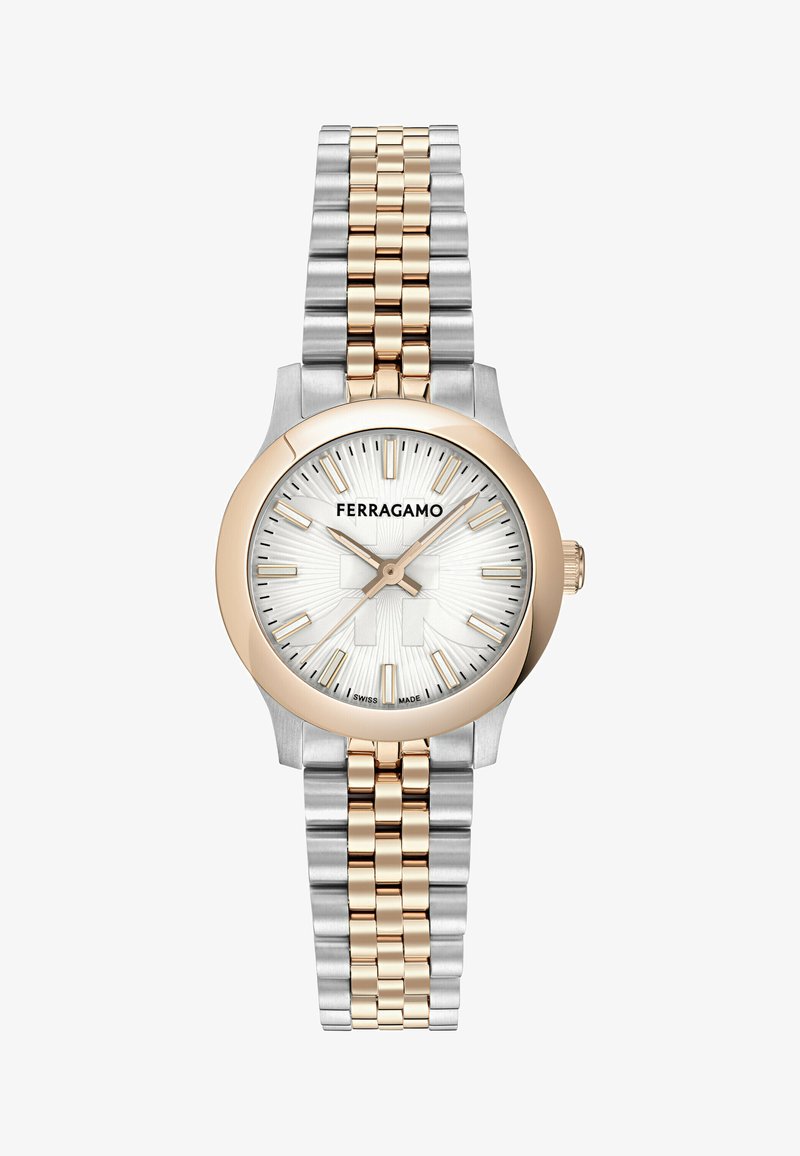 Suds un zelta toņu pulkstenis ar apaļu korpusu, baltu teksturētu ciparnīcu un apzīmētām stundu rādītājām; tam ir divu toņu metāla siksna.