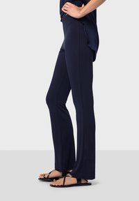 Marinafärgade flare tights i mjukt, elastiskt tyg med en slät yta. Bärs med svarta platta sandaler med minimalistiska band och dekorativa inslag.