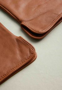 Brown leather gloves with a smooth texture, rounded edges, and contrasting stitching. The gloves are partially folded, revealing their shape.