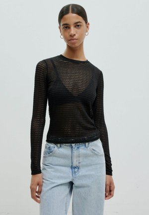 Schwarzes langärmliges Mesh-Top mit rundem Ausschnitt und figurbetontem Design, kombiniert mit hellblauen hochgeschnittenen Jeans.