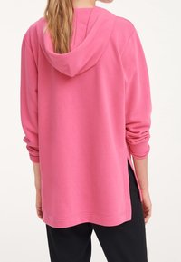 Felpa rosa con cappuccio, maniche lunghe, fessure laterali e vestibilità rilassata. Realizzata in tessuto morbido. Dettagli di cucitura visibili sull'orlo.