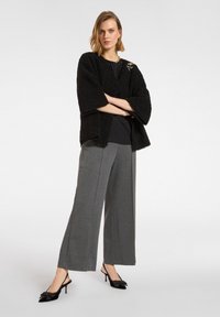 Czarna kurtka o teksturowanej powierzchni z szerokimi rękawami, noszona na czarnej bluzce. W połączeniu z szarymi spodniami o szerokich nogawkach oraz czarnymi szpilkami z zapięciem z tyłu i detalem w postaci kokardy.