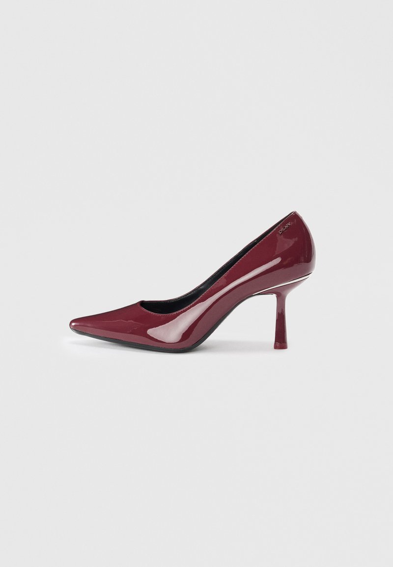 Spīdīgi bordo augstpapēžu kurpes ar smailu purngalu un šauru stiletto papēdi, redzams zīmola logo pie papēža, fona krāsa - gaiši pelēka.