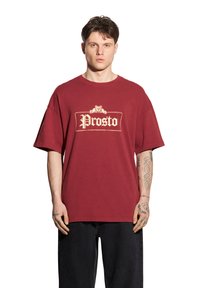 Bordowa bawełniana koszulka z krótkim rękawem, z beżowym logo "Prosto" w prostokątnej ramce na przodzie.