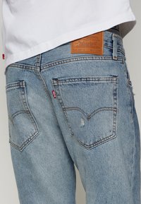 Ljust blå denimjeans har en klassisk design med synliga sömmar och två bakfickor, en med en liten frans och en lädermärkning.