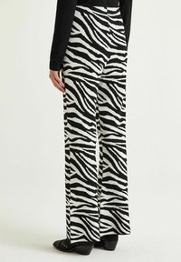 Pantalon à jambes larges en tissu doux avec un motif rayé zèbre noir et blanc. Il présente une taille haute et des poches inclinées. Chaussures à talons noires.