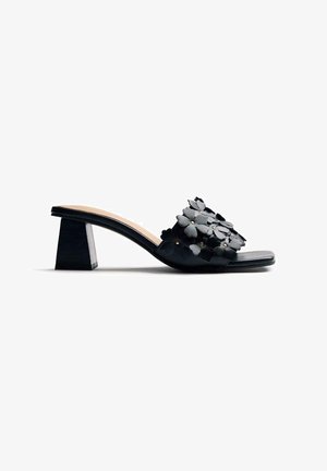 Sandalia negra de tacón medio con punta cuadrada y apliques florales decorativos en 3D a lo largo de la tira sobre el pie.