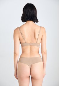 Béžový bikiny set s měkkou texturovanou tkaninou. Podprsenka má nastavitelné ramínka a háčkové zapínání, doplněné o odpovídající minimalistické spodní prádlo.