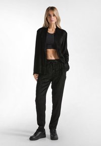 Zwart corduroy loungewear set met een ontspannen fit blazer en broek met een elastische tailleband, aangevuld met een cropped top en zwarte sneakers.