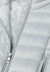Šviesiai pilkas pūkinis švarkas su lygia, blizgia išorine danga. Yra horizontaliai quilted sekcijos ir sidabrinė priekinė užtrauktukas. Vidus puošia minkšta pamušalo medžiaga.