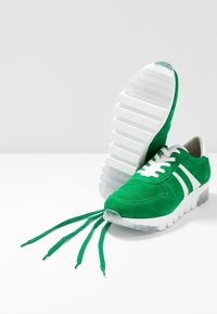 Sneaker in suede verde con accenti bianchi, punta perforata e lacci allungati unici. Suola spessa in gomma bianca e traslucida.