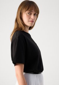 Svart T-skjorte med korte ermer, klassisk rund hals og avslappet passform. Har en subtil Lacoste-logo på kanten. Minimalistisk design.