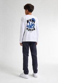 Witte lange mouwen t-shirt met een kleurrafische opdruk met de tekst "Miami Florida" in blauw en zwart. Gecombineerd met donkere broek en witte sneakers.