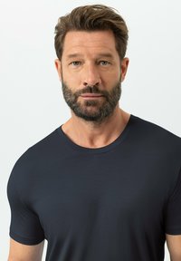 T-shirt bleu foncé à col rond en tissu lisse, avec manches courtes et silhouette ajustée, présentant des détails de design minimalistes.