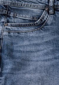 Denim-Jeans in einem hellblauen Waschton mit dezentem Verblassen. Zu den Merkmalen gehören eine Gesäßtasche, geschwungene Nähte und metallische Knopfdetails.