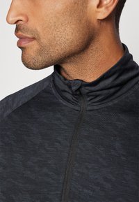 Chaqueta de atletismo negra con cuello de cremallera, presenta un patrón texturizado, cierre frontal de cremallera hasta la cuarta parte y un silueta ajustada.
