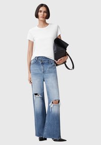 T-shirt bianco a girocollo, jeans a gamba larga in lavaggio chiaro con orlo sfilacciato e strappi al ginocchio, che tiene una borsa nera con una trama testurizzata.