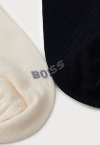 Due calzini, uno color crema e uno color navy, con una texture a coste e un sottile logo "BOSS" grigio sul calzino navy.