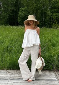 Biała, zwiewna bluzka bez rękawów z elastycznym dekoltem, zestawiona z beżowymi spodniami w pasy o szerokich nogawkach. W zestaw wchodzi także szerokokątny słomkowy kapelusz i pleciona torba.