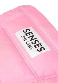 Bereich mit rosafarbener Steppjacke, die ein weißes Etikett mit schwarzem Text "SENSES THE LABEL" zeigt. Glatte Textur mit gesteppter Naht.