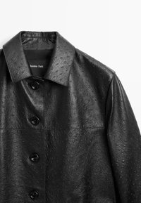 Zwarte leren jas met een gestructureerde oppervlakte, voorzien van een gespreide kraag, knopen aan de voorkant en een gladde voering.