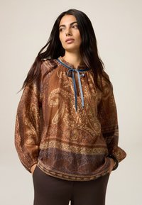 Braun bedruckte Bluse mit Paisleymuster, Kordelzug im Ausschnitt, langen Ärmeln und elastischen Bündchen. Sie zeichnet sich durch einen glatten Stoff und eine kontrastierende blaue Schleife aus.