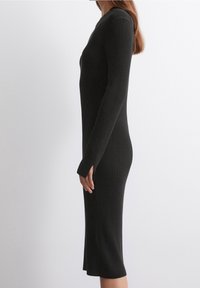 Robe à manches longues en noir, avec une silhouette ajustée, des fentes latérales et un col rond, fabriquée à partir d'un tissu en tricot doux.