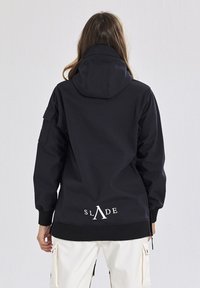 Marineblå huvjacka med avslappnad passform, i strukturerat tyg, med ribbade ärmmuddar och en vit logotyp på baksidan. Sidofickor med dragkedja ingår.