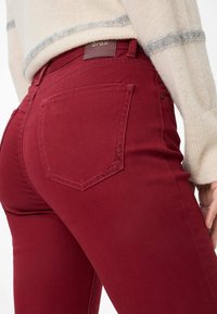 Jeans di denim rossi con vestibilità slim, dotati di un'etichetta in pelle marrone e cuciture decorative sulla tasca posteriore.