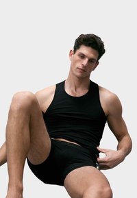 Černé tílko z hladké látky, doplněné černými těsně přiléhajícími boxerkami, představující jednoduchý design a úzký střih.