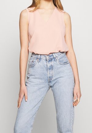 Top senza maniche in rosa pallido con scollatura a V, in tessuto leggero e vestibilità rilassata, abbinato a jeans in denim azzurro chiaro a vita alta.