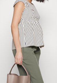 Pruhované těhotenské tričko v krémové a námořnické modři, s krátkými rukávy a peplum střihem. V kombinaci se zeleno-olivovými kalhotami a taškou v taupe.