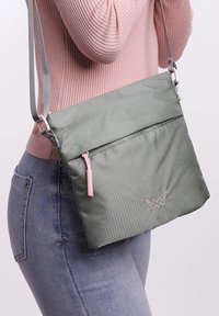 Grüne Nylon-Crossbody-Tasche mit strukturiertem Finish, pinkem Reißverschluss-Anhänger und Logo-Akzent. Verstellbarer Riemen und Frontreißverschluss-Tasche inklusive.