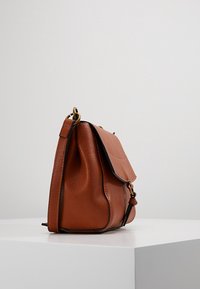 Borsa a tracolla in pelle marrone con chiusura a patta, caratterizzata da una texture liscia, forma arrotondata, dettagli in metallo dorato e una tracolla corta.